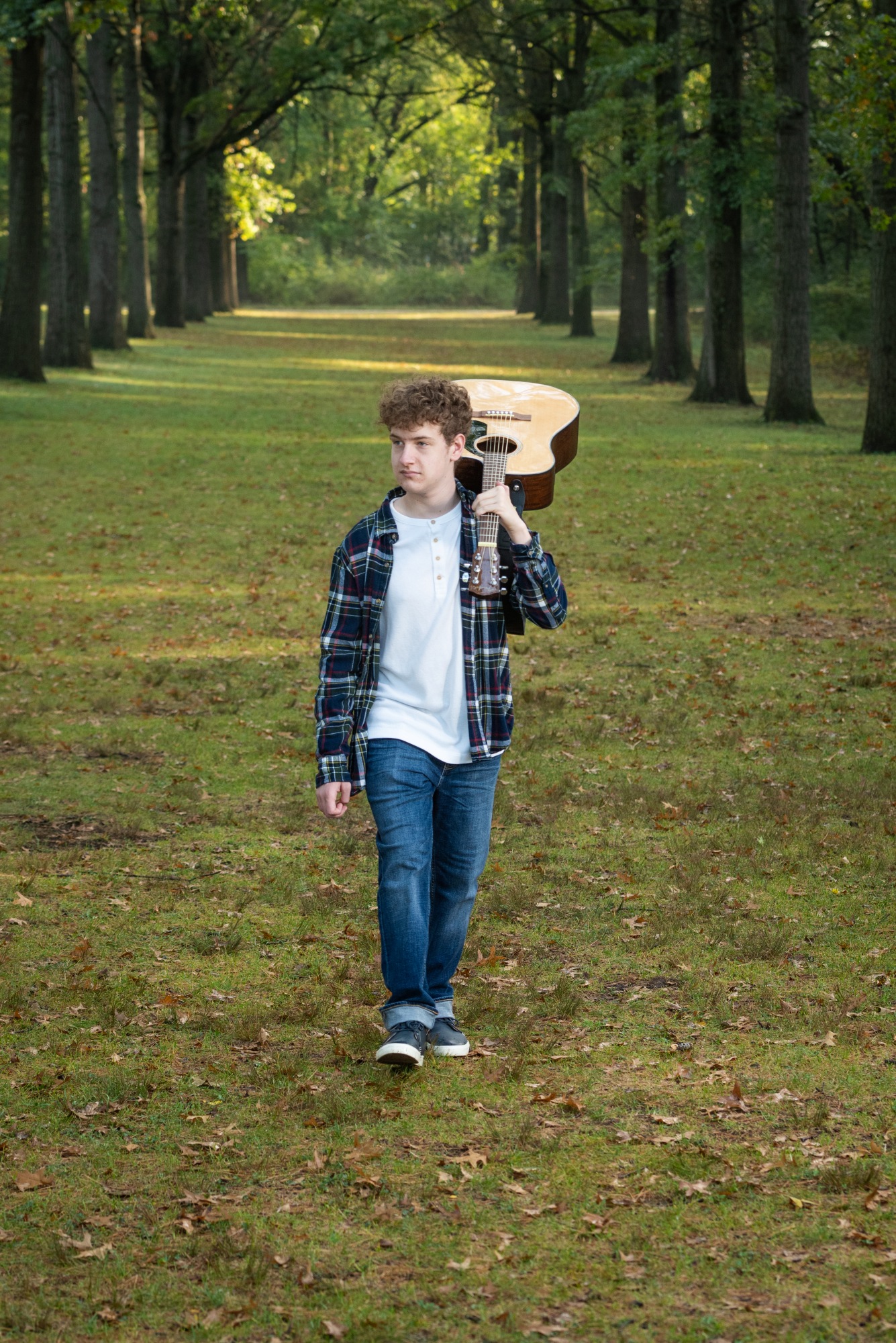 Outdoor Senior portrait. A casual young man walking outdoors with his guitar over his shoulder.