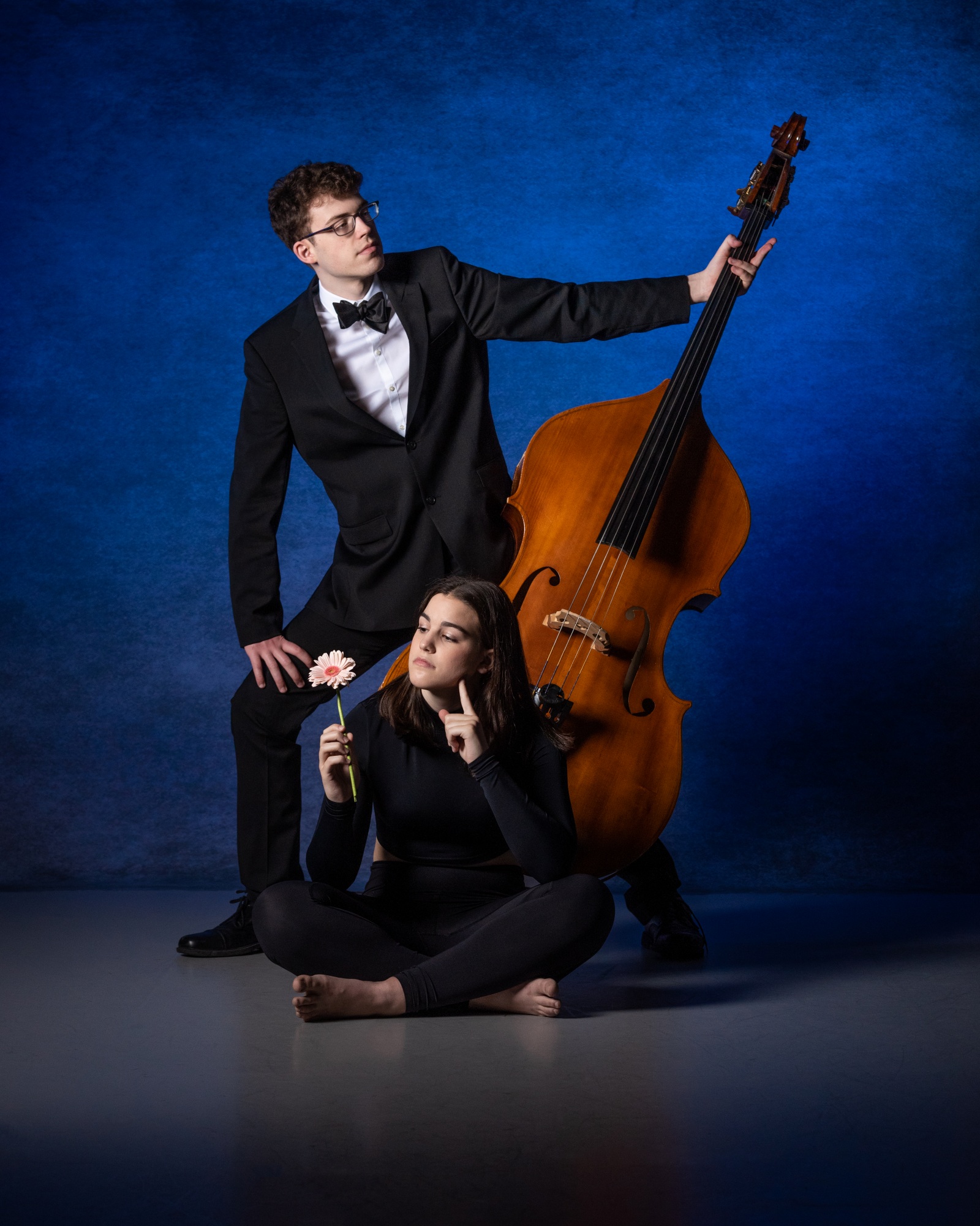 Formal portrait of a bass player and sibling. Young man is standing and his sister is seated.